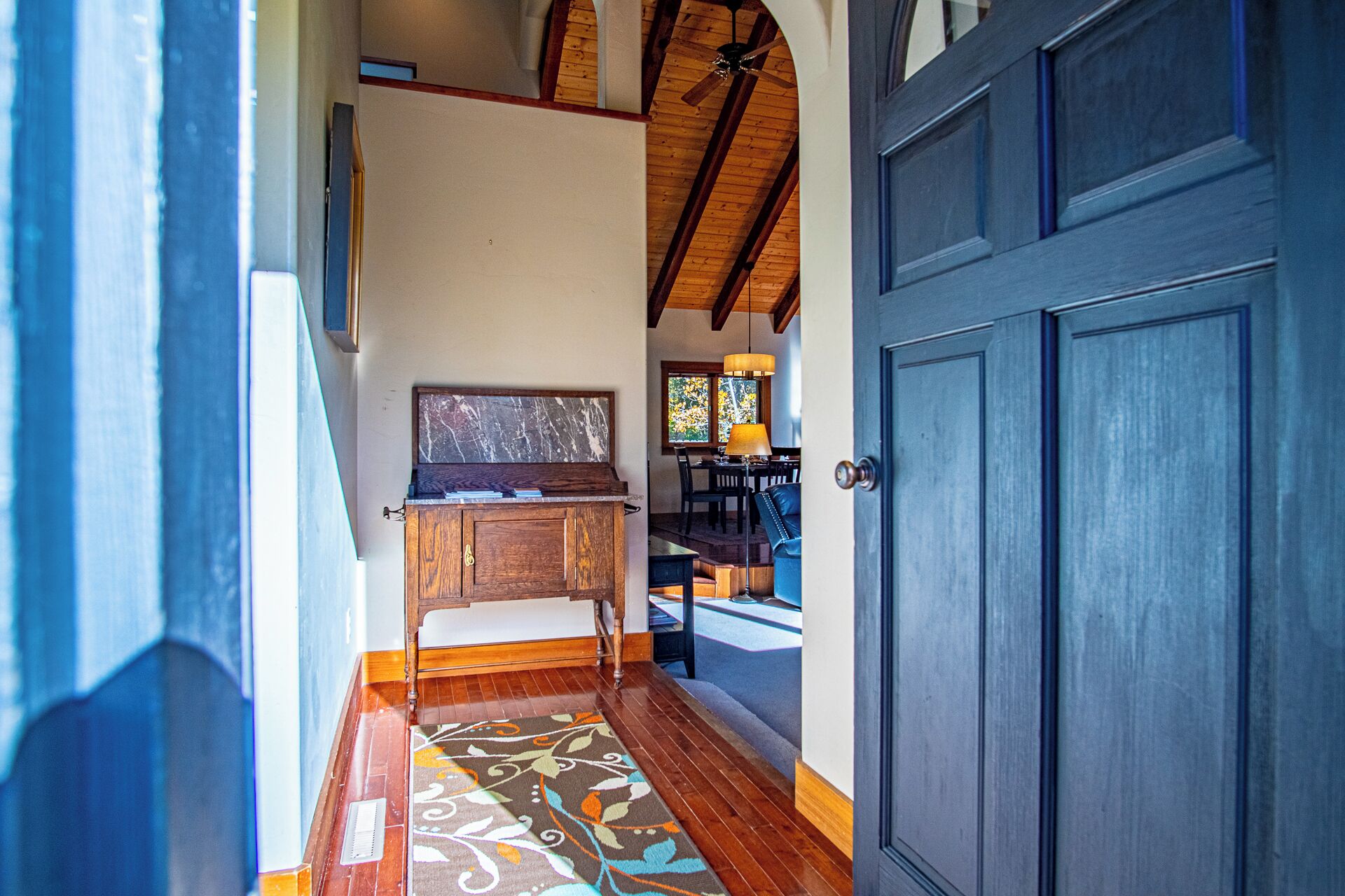 A hallway with a wooden floor, a patterned rug, a wooden cabinet, and a blue door.