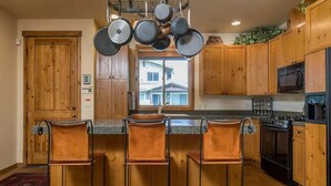 Cozinha com armários de madeira, uma ilha central com banquetas, micro-ondas, fogão e panelas penduradas.