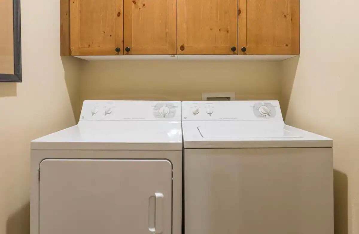 A laundry area with two white washing machines and wooden cabinets above.