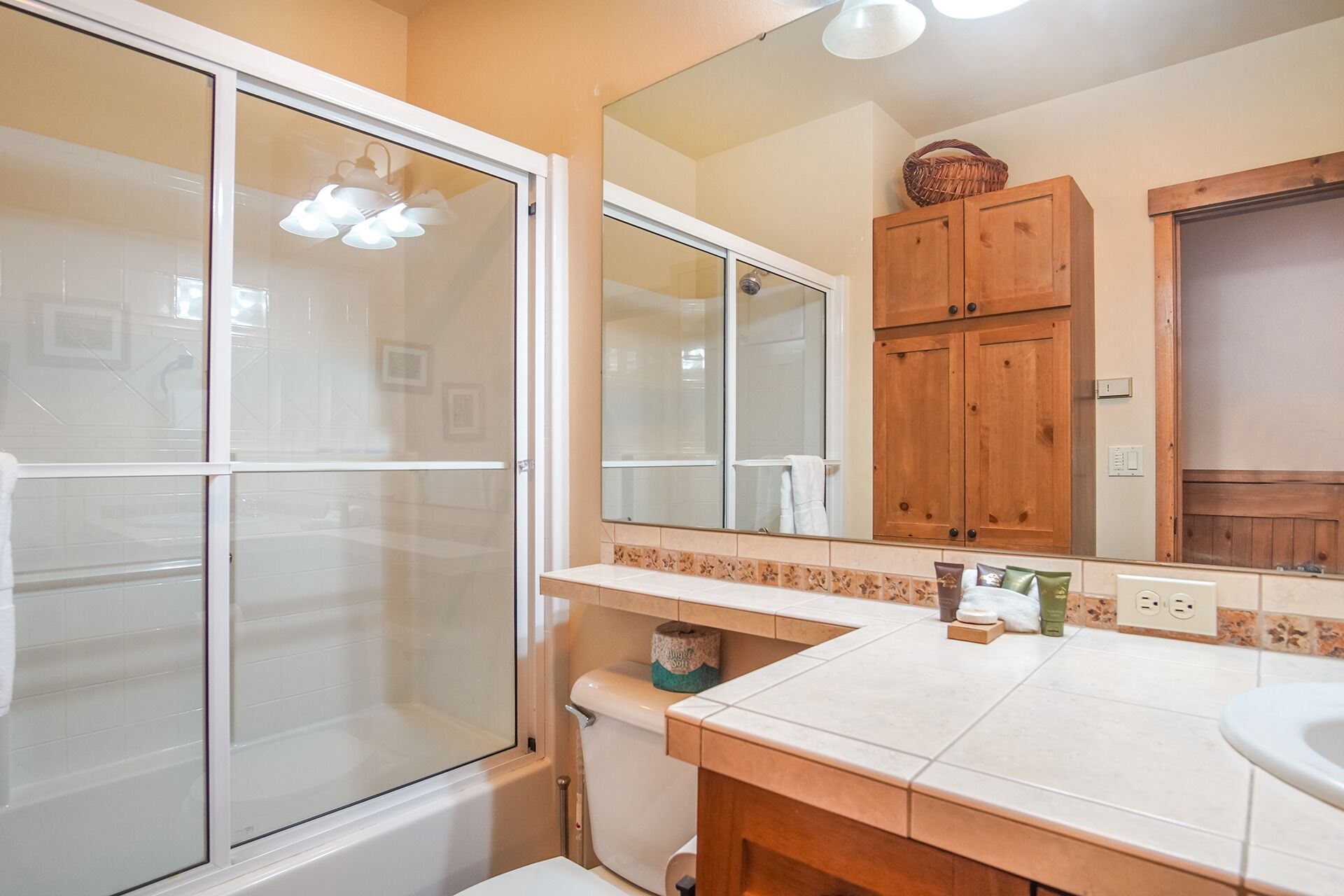 A bathroom with a glass shower enclosure, a toilet, a sink with a mirror, and wooden cabinets.
