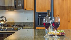 Uma cozinha com micro-ondas, fogão e um armário de madeira. Há duas taças de vinho tinto no balcão, uma garrafa de vinho e um prato com uvas e bolachas.