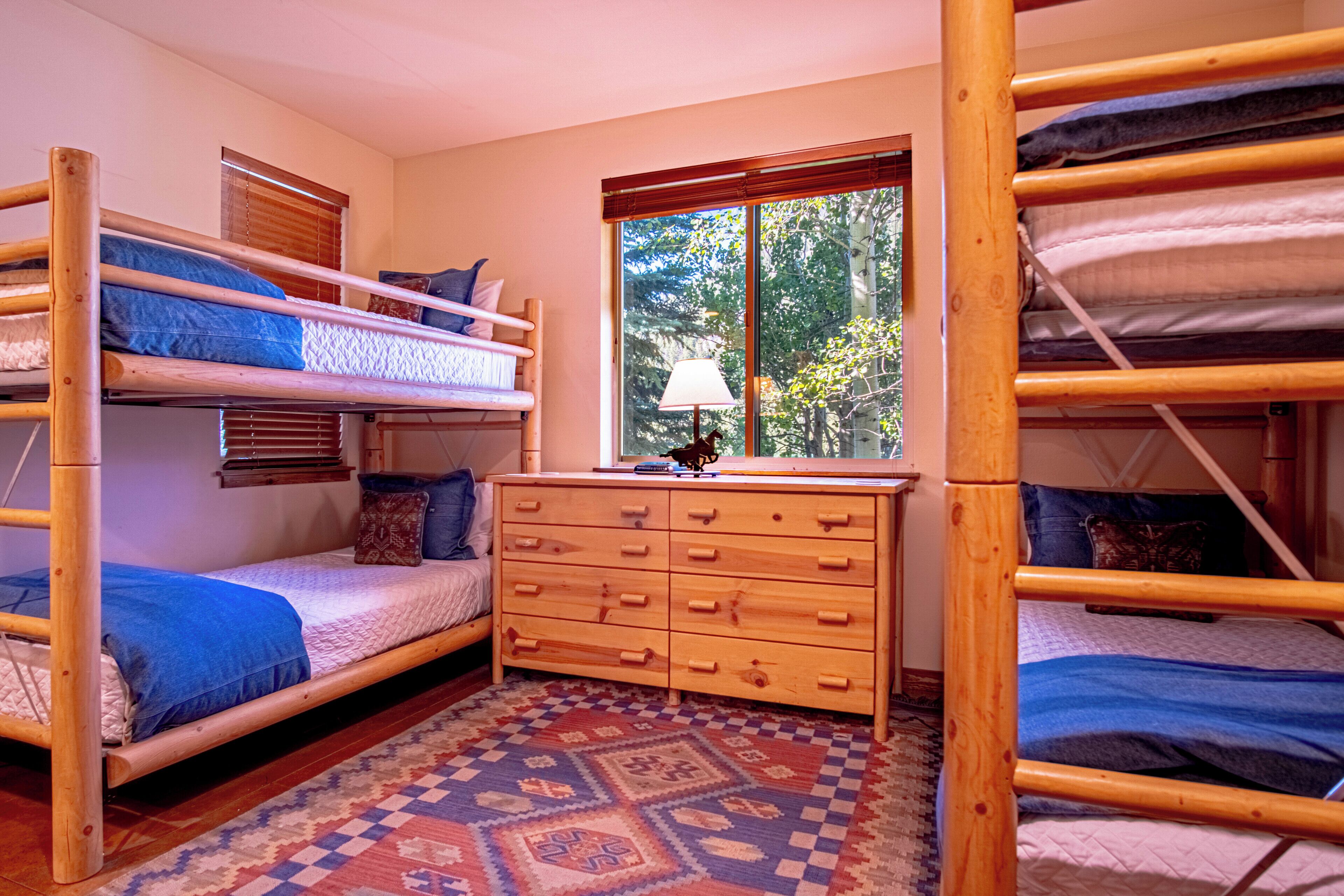 A room with bunk beds, a wooden dresser, and a window with a view of trees.
