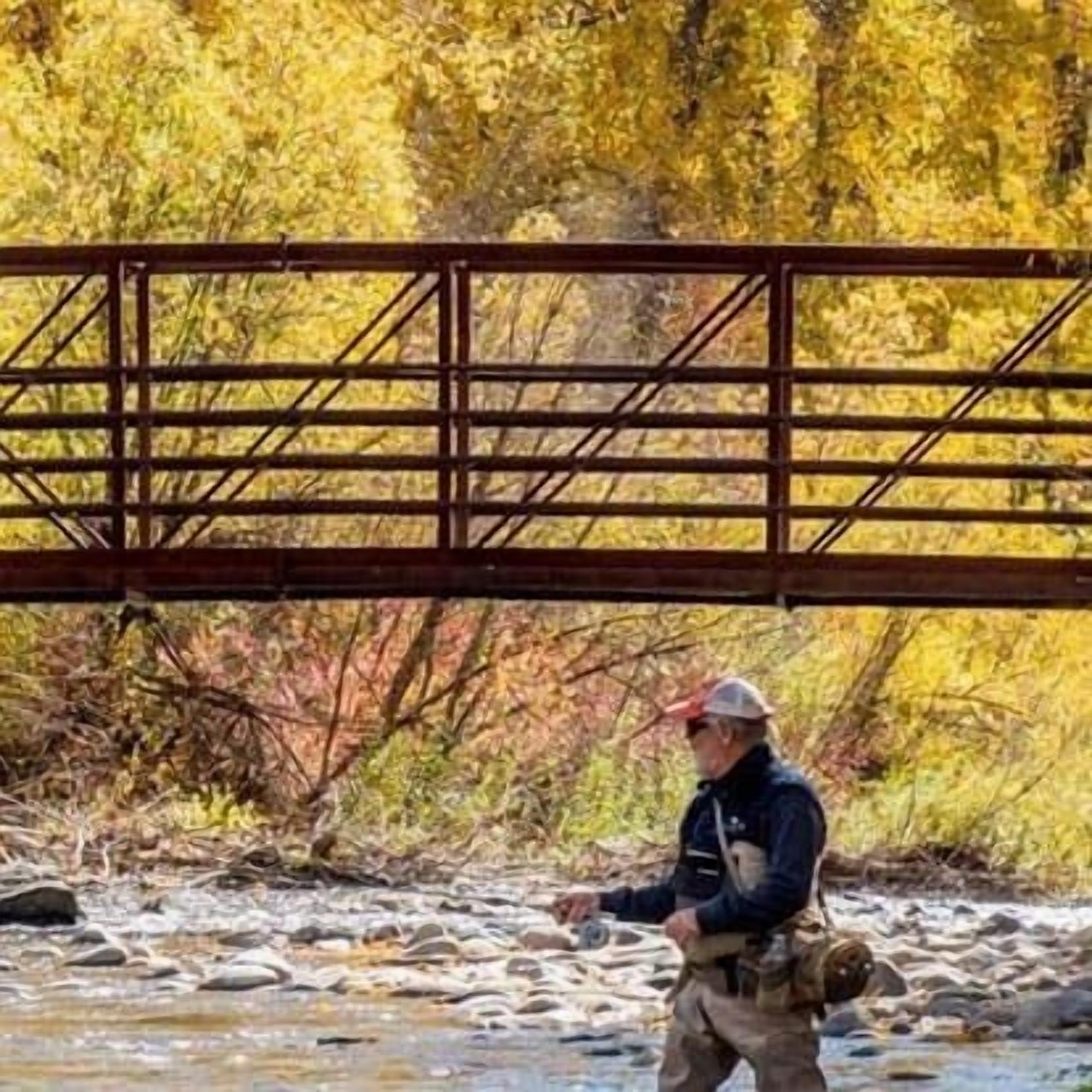 A person crossing a bridge over a river with autumn foliage in the background.