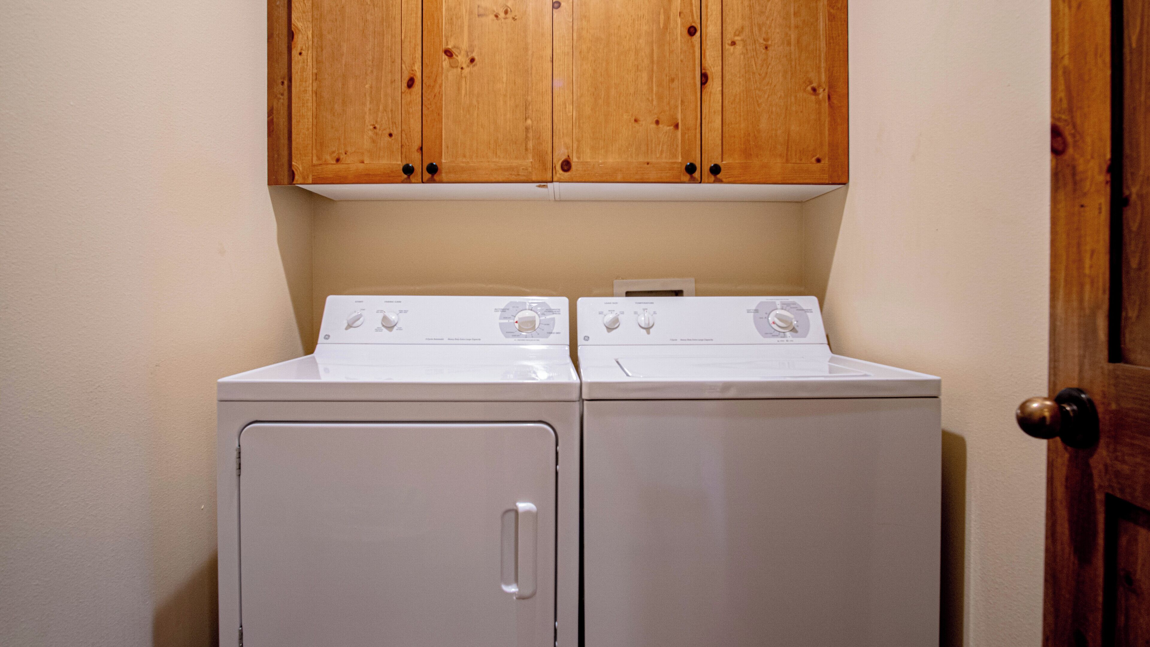 A laundry room with two white washing machines and wooden cabinets above.