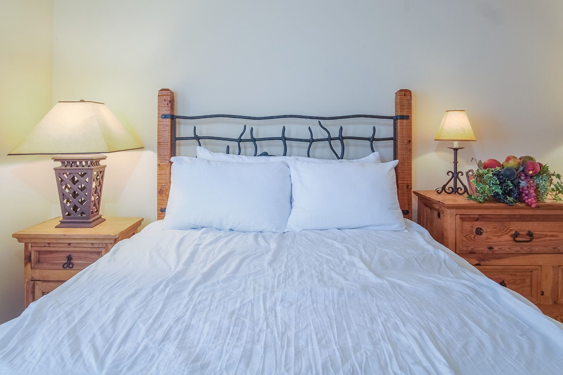 A bed with white linens, two bedside tables with lamps, and a wooden nightstand with a plant.