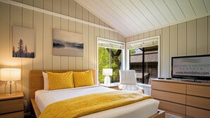 Une chambre d’hôtel avec un grand lit, une télévision, un bureau avec une lampe et une fenêtre donnant sur des arbres.