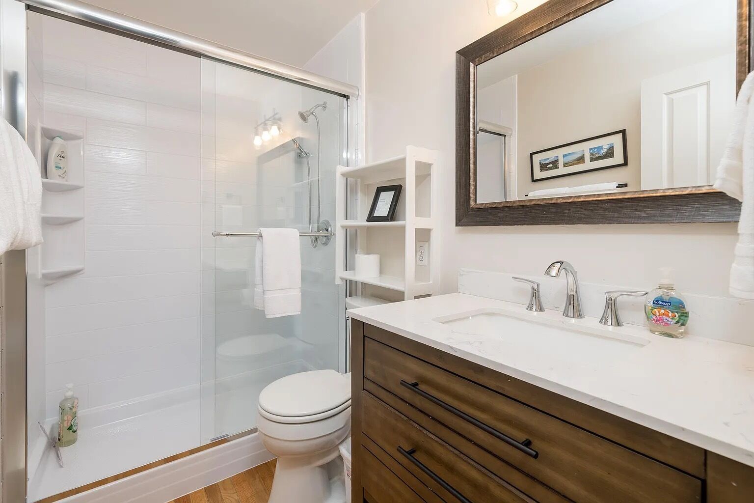 A modern bathroom with a glass-enclosed shower, a white toilet, a vanity with a large mirror, and wooden cabinetry.