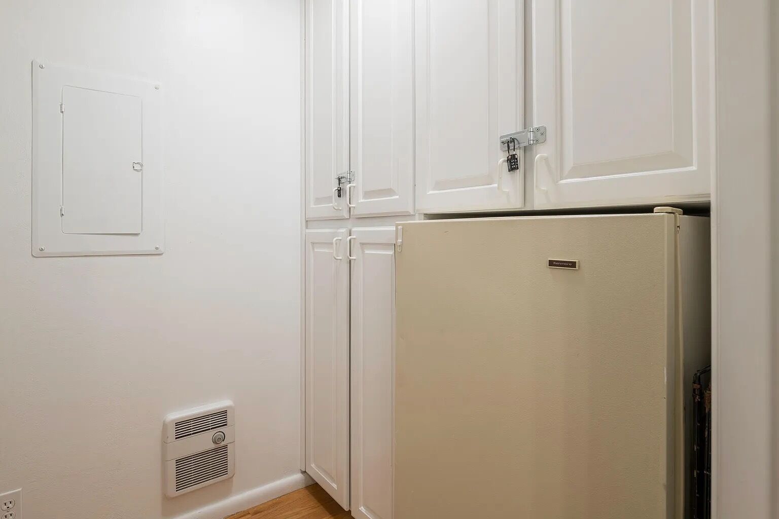 Une petite cuisine avec des meubles blancs, un réfrigérateur blanc et une hotte fixée au mur.