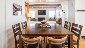 A dining area with a wooden table and chairs, a bowl of bread, and a fireplace in the background. - 3BD Downtown Ketchum Condo - Near Town & Ski Lifts (Ketchum)