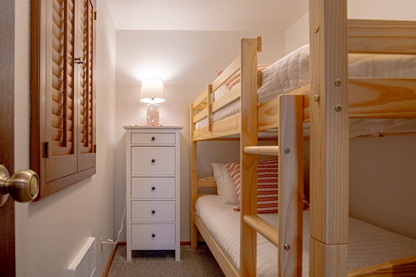 A bunk bed room with a white dresser and a lamp.