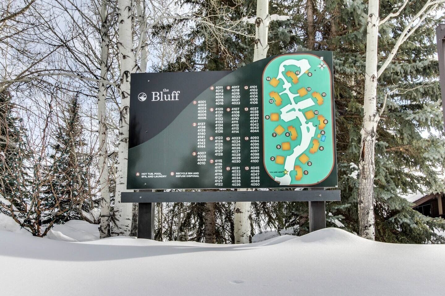 A snow-covered sign with a map and a list of room numbers for The Bluff hotel.