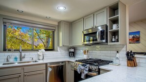 A modern kitchen with grey cabinets, a stainless steel range, a microwave, and a window with a view of trees. - Ridge Condo - Luxury Condo W/resort Amenities (Sun Valley)