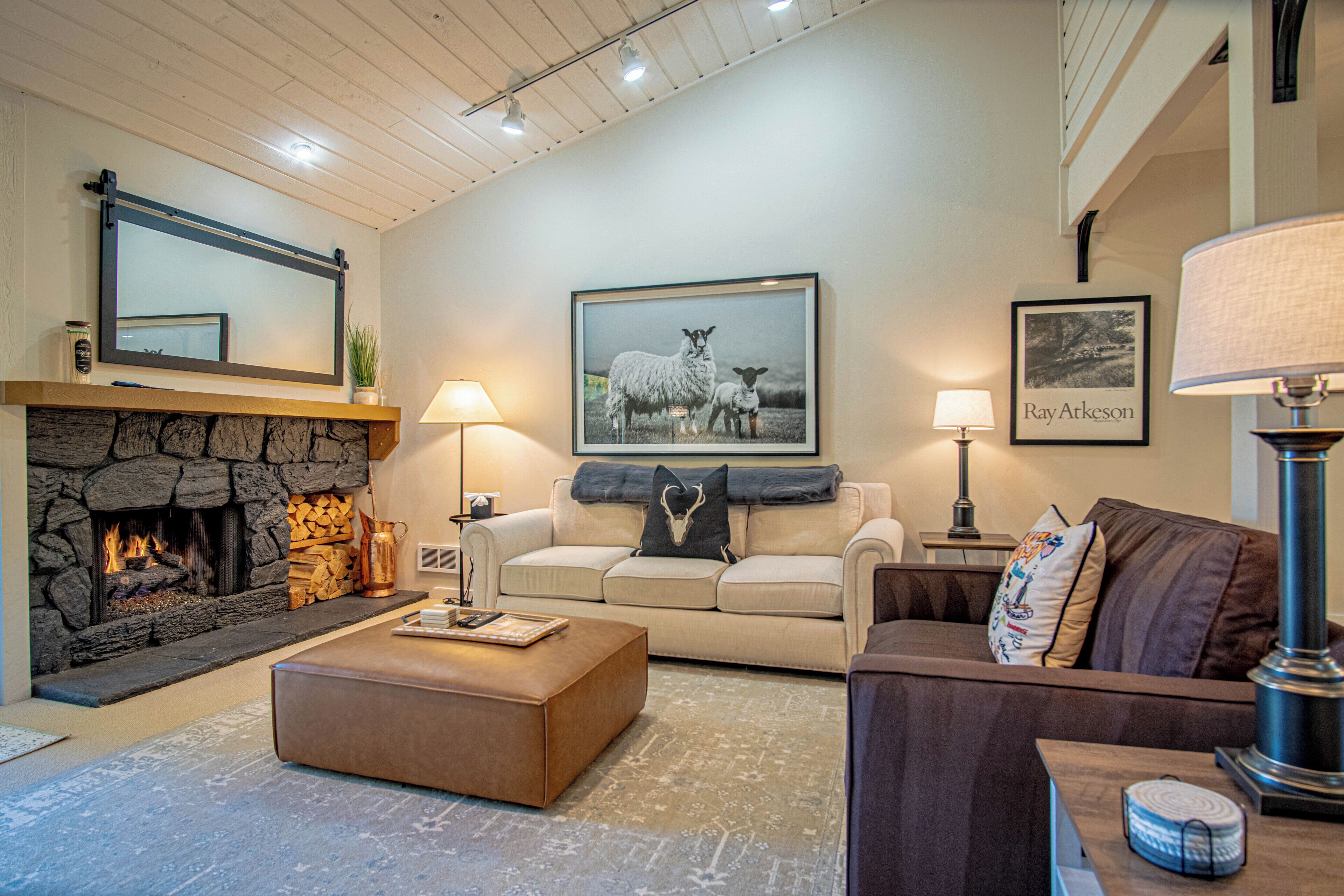 A cozy living room with a stone fireplace, a large framed picture of sheep, and a lamp on a side table.