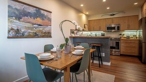 A modern kitchen with wooden cabinets, a central island, and a dining area with a table set for four. - 2bd, 2BA Ketchum Condo Newly Remodeled & Central (Ketchum)