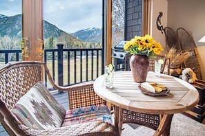 A wooden deck with a wicker chair and a table with a vase of sunflowers, a grill, and a view of mountains. - C21 Bigwood - Stunning Baldy Views (Ketchum)