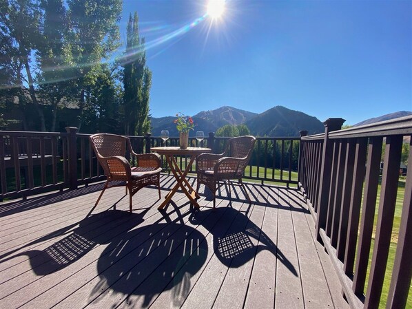 Une terrasse en bois, agrémentée de chaises et d’une table en osier, qui offre une vue sur un paysage montagneux.