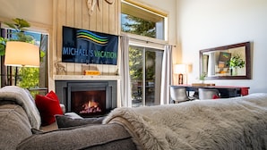 A cozy room with a fireplace, a television displaying 'Michael's Vacation Rentals', and a view of the outdoors. - Bonne Vie 2233 in the Heart of Elkhorn With Resort Amenities (Sun Valley)