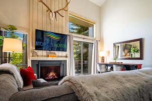 Um quarto aconchegante com lareira, uma televisão exibindo 'Michael's Vacation Rentals' e vista para o exterior.