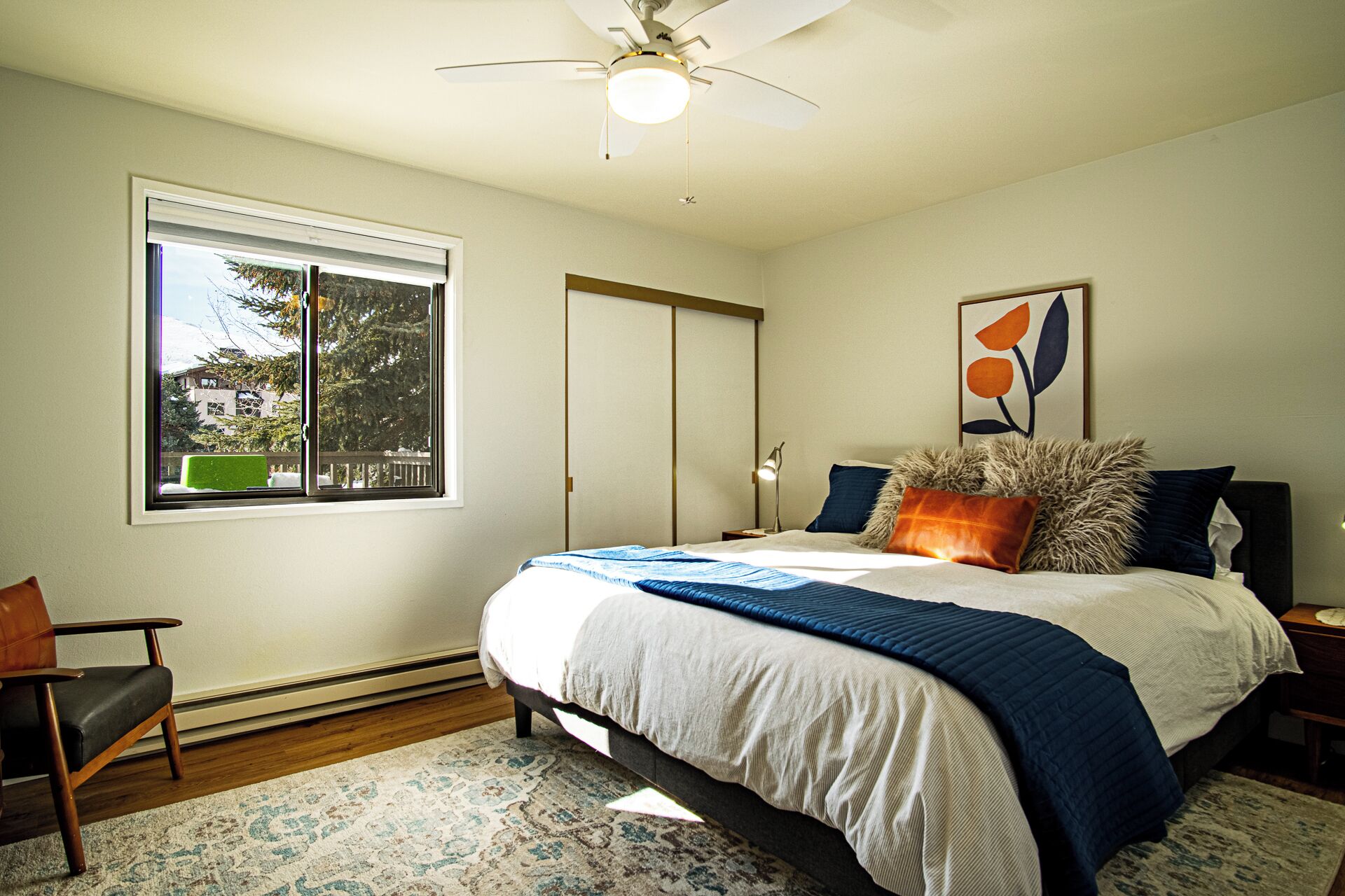 A bedroom with a bed, a chair, a window, a door, and a ceiling fan.