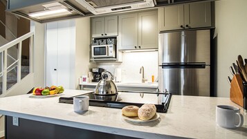 Uma cozinha moderna com uma geladeira de aço inoxidável, um micro-ondas e uma chaleira sobre o balcão.