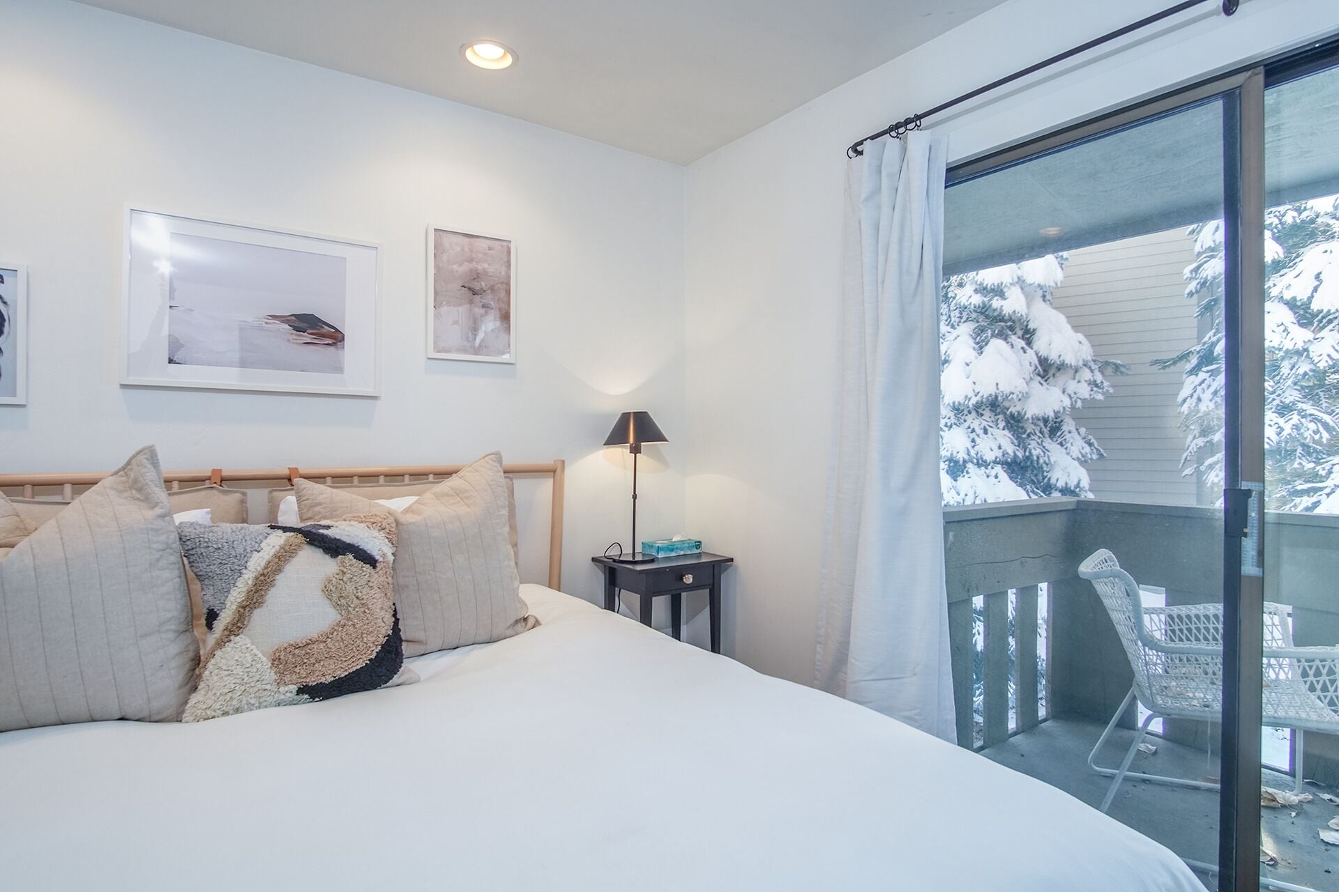 A bedroom with a bed, a nightstand, a lamp, and a view of a snowy balcony.