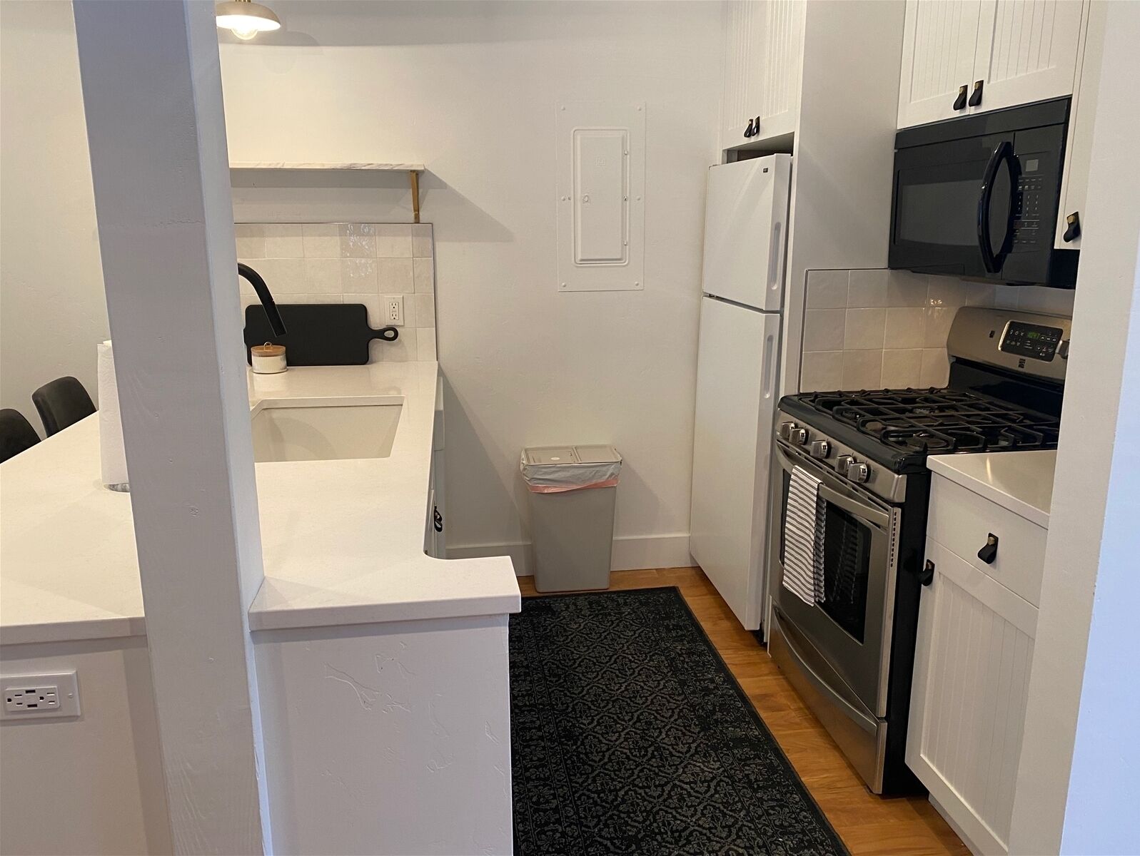 A compact kitchen with white cabinetry, a black stove, a microwave, and a refrigerator.