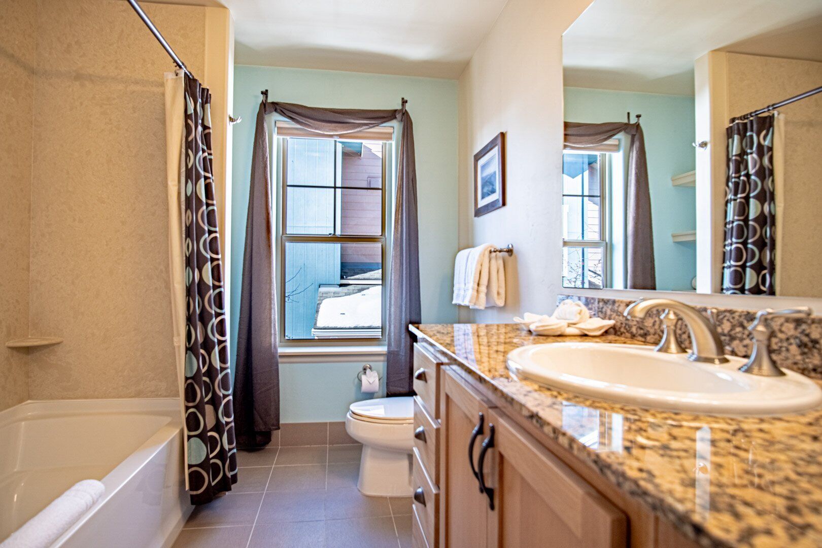 Un baño con bañera, inodoro, lavabo y ventana con cortinas.