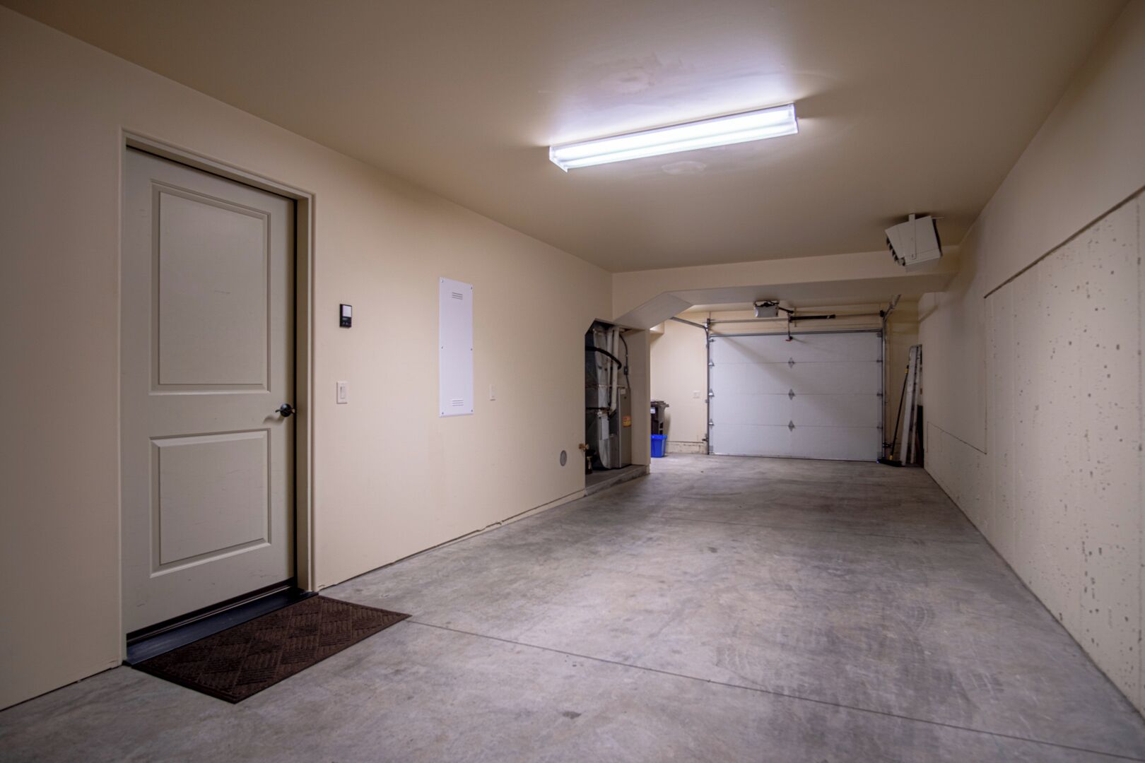 A clean, empty garage with a fluorescent light, a door, and a blue trash bin.