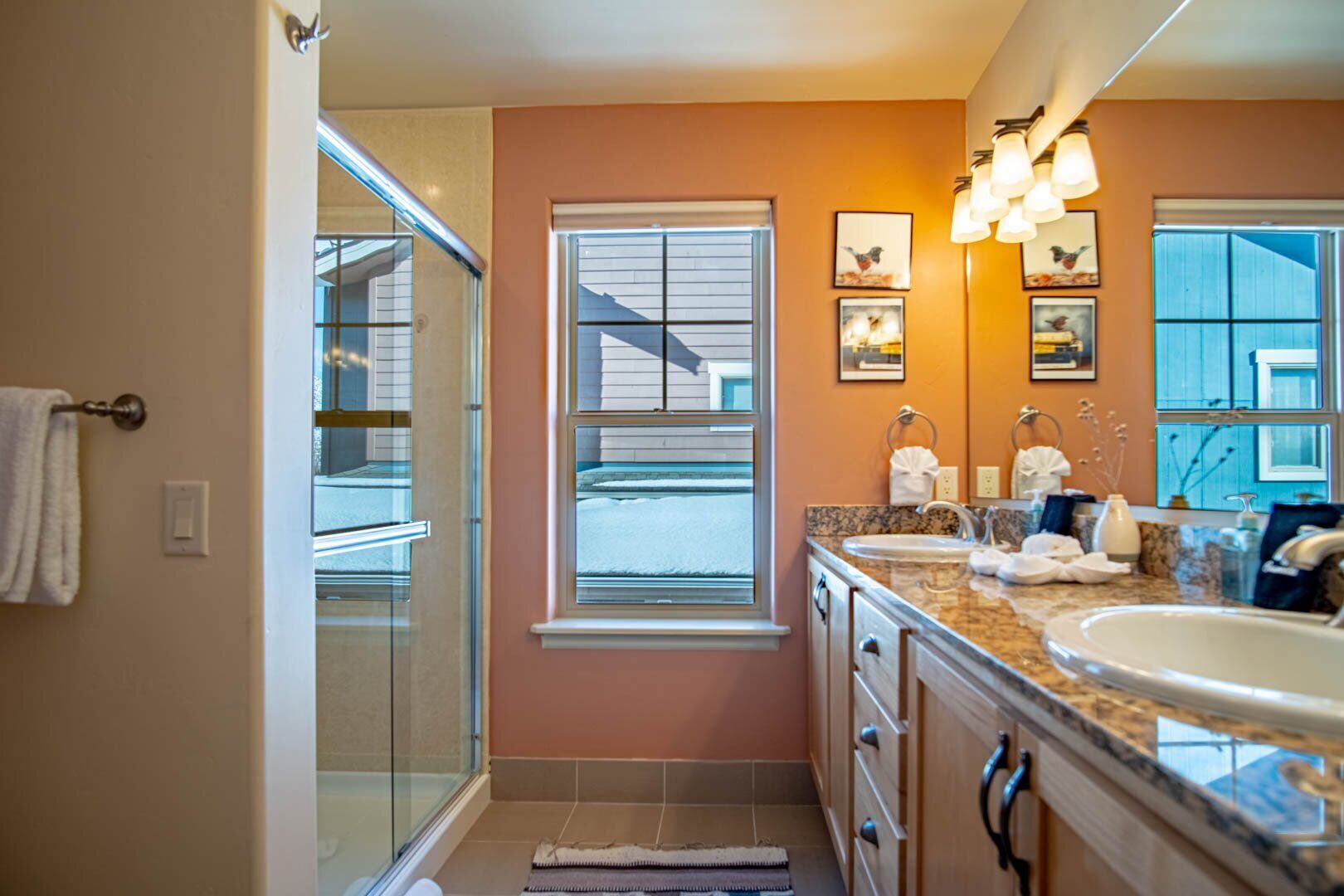 A bathroom with a glass shower, a vanity with a sink, and a window.