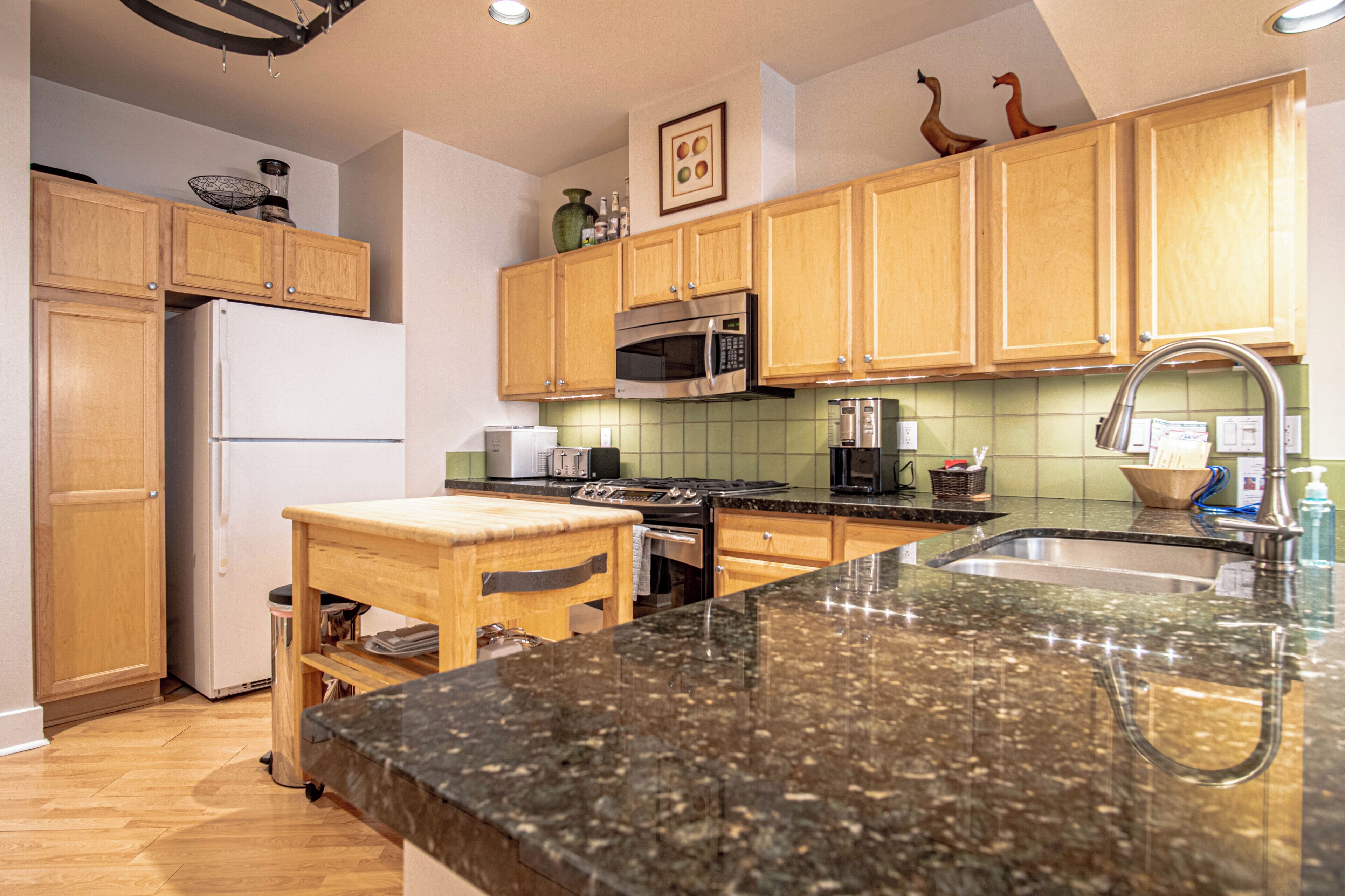A kitchen with wooden cabinets, a stainless steel microwave, a sink, and a granite countertop.