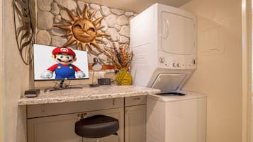 A kitchen with a stone wall, a washing machine, a Mario-themed monitor, and a bar stool.