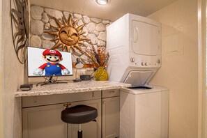 A kitchen with a stone wall, a washing machine, a Mario-themed monitor, and a bar stool. - Snow Run Haven #8 (Ketchum)