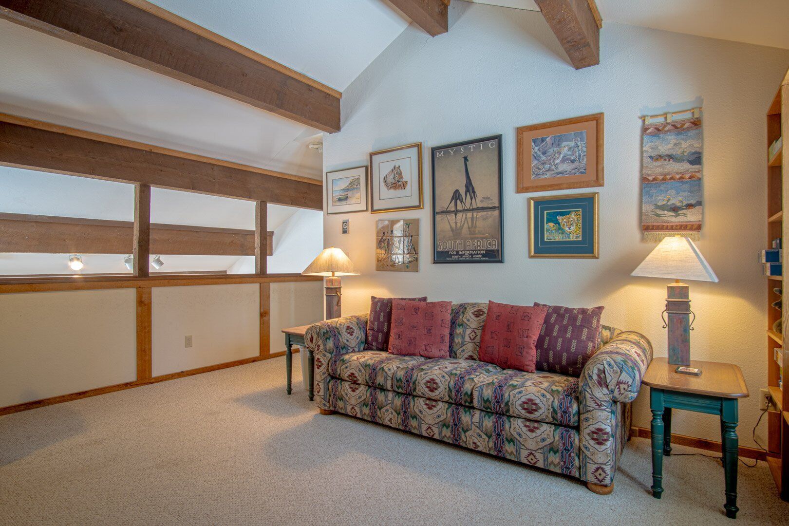A cozy living room with a patterned sofa, wooden beams, and wall art including a giraffe and a South Africa poster.