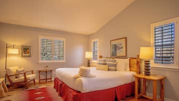 A bedroom with a large bed, two bedside tables, a chair, and a window with blinds.