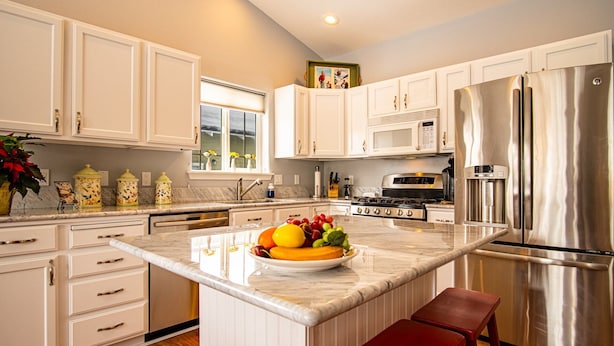 A modern kitchen with white cabinetry, stainless steel appliances, and a marble island with a fruit bowl. - In the Heart of Hailey; Private Pet-friendly 3 Bedroom Home With Garage (Hailey)