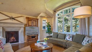 A spacious living room with a fireplace, a large window, and a ceiling fan. - Chateau Du Soleil- Luxury Home Near Ski Lifts & Downtown Ketchum! (Ketchum)