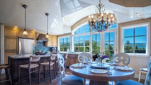 A spacious kitchen with a large island, wooden cabinetry, and a dining area with a round table and chairs. - Chateau Du Soleil- Luxury Home Near Ski Lifts & Downtown Ketchum! (Ketchum)