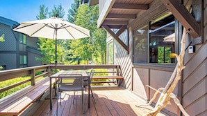 A wooden deck with a table and chairs, a bench, and a large umbrella. - Wildwood Cottage at Villager + SV Resort Amenities (Sun Valley)