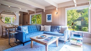 A cozy living room with a blue sofa, wooden coffee table, and a dining area with a wooden table and chairs. - Wildwood Cottage at Villager + SV Resort Amenities (Sun Valley)
