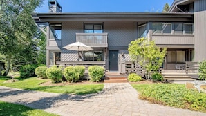 A modern two-story house with a covered front porch, a small balcony, and a well-maintained garden. - Wildwood Cottage at Villager + SV Resort Amenities (Sun Valley)
