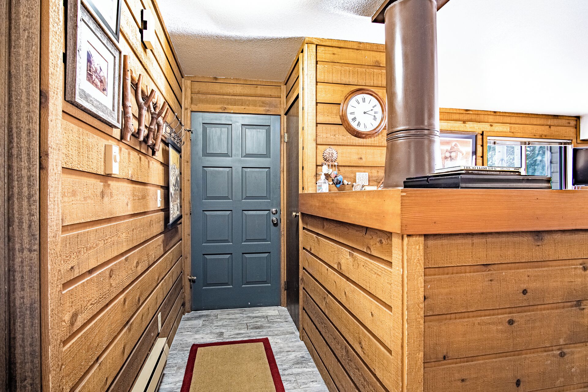 A narrow hallway with wooden walls, a blue door, and a wooden counter with a clock.