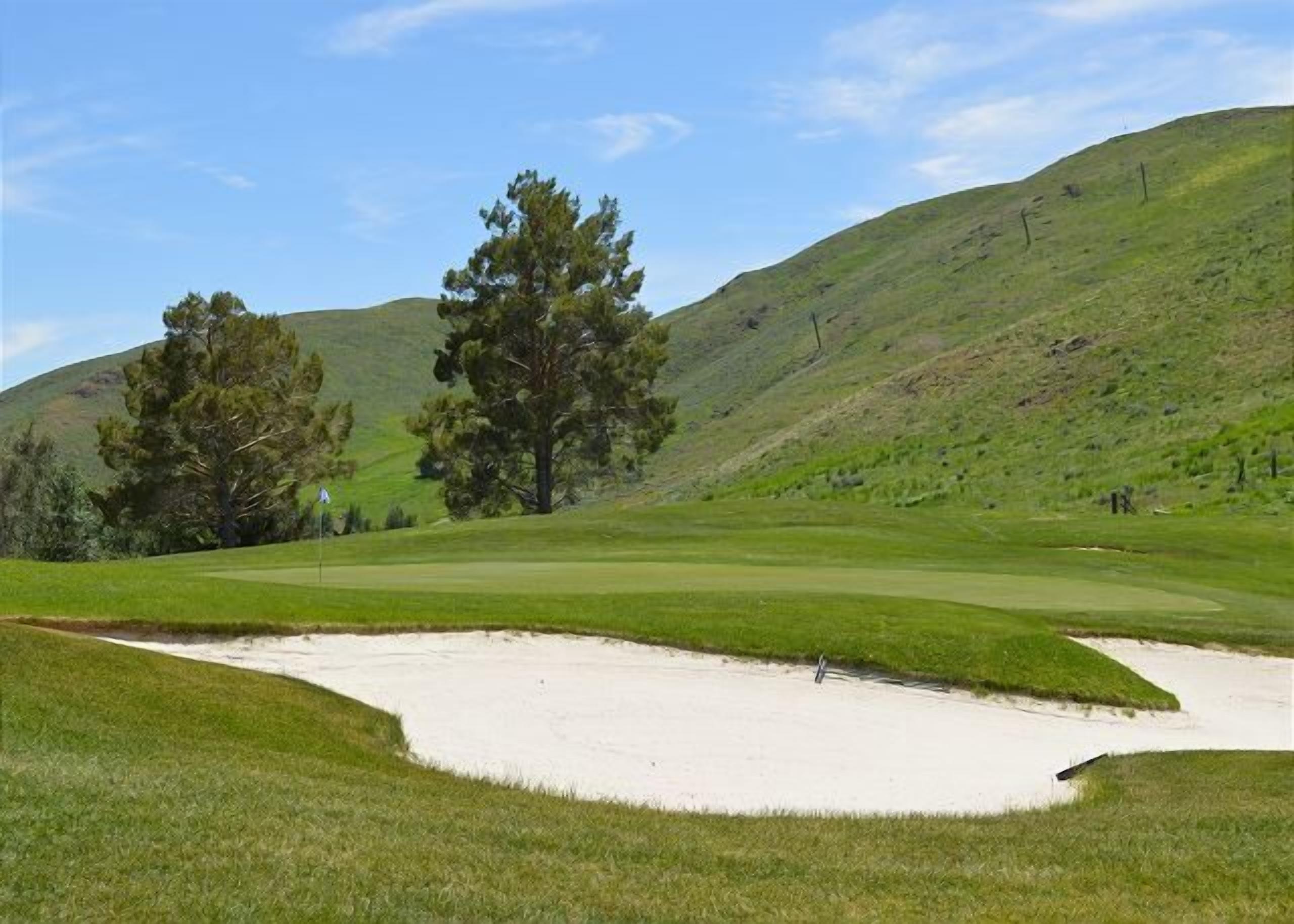 Un campo de golf con búnkeres de arena, árboles y un terreno ondulado.