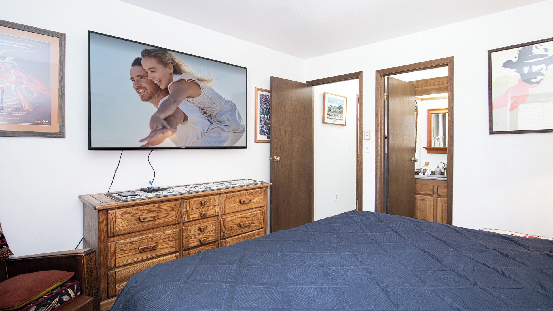 Une chambre à coucher avec un grand lit, une commode en bois et un téléviseur fixé au mur.