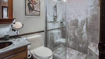 A bathroom with a glass shower enclosure, a toilet, a vanity with a mirror, and a wall-mounted picture.