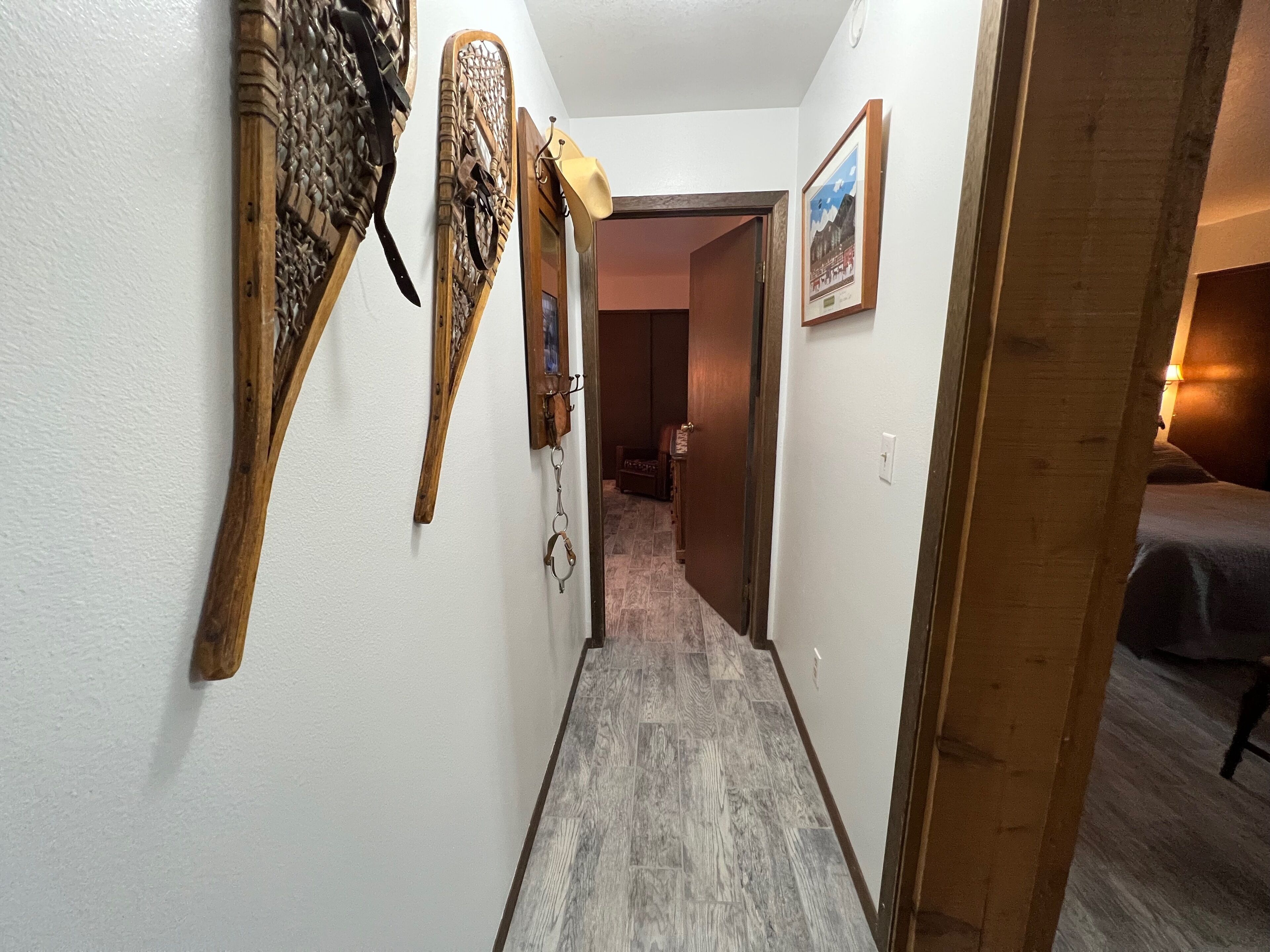 A narrow hallway with wooden wall decorations, a door leading to a room with a bed, and a framed picture on the wall.