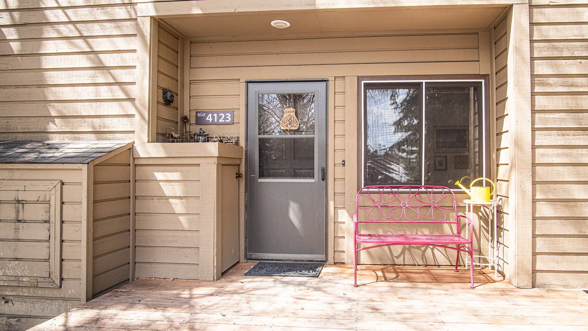 A house with a front door labeled "4123," a small porch with a pink metal bench, and a window to the right.
