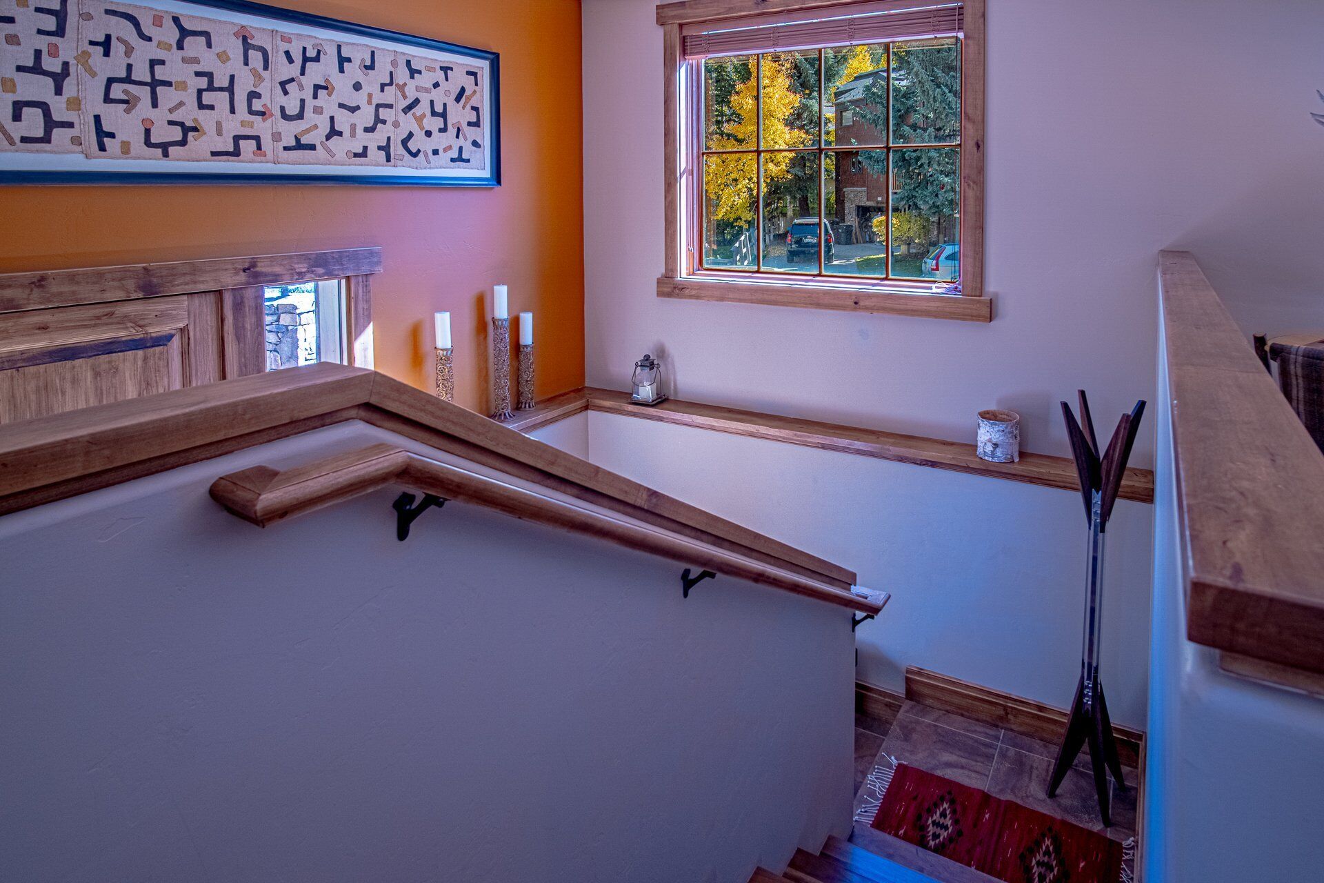 A staircase with wooden handrails, a window with a view of trees, and a wall-mounted decorative piece.