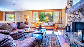 A spacious living room with a leather sofa, a coffee table, and a stone fireplace. - Lux Baldy Vista at Warm Springs Home + Hot Tub - Walk to SV Ski Lifts (Ketchum)