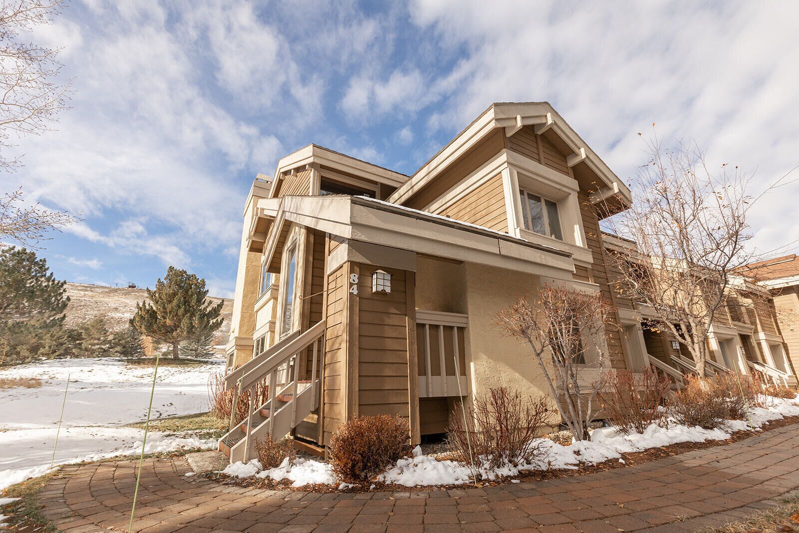 A two-story house with a front porch, a staircase leading to the entrance, and a number '84' sign on the side.