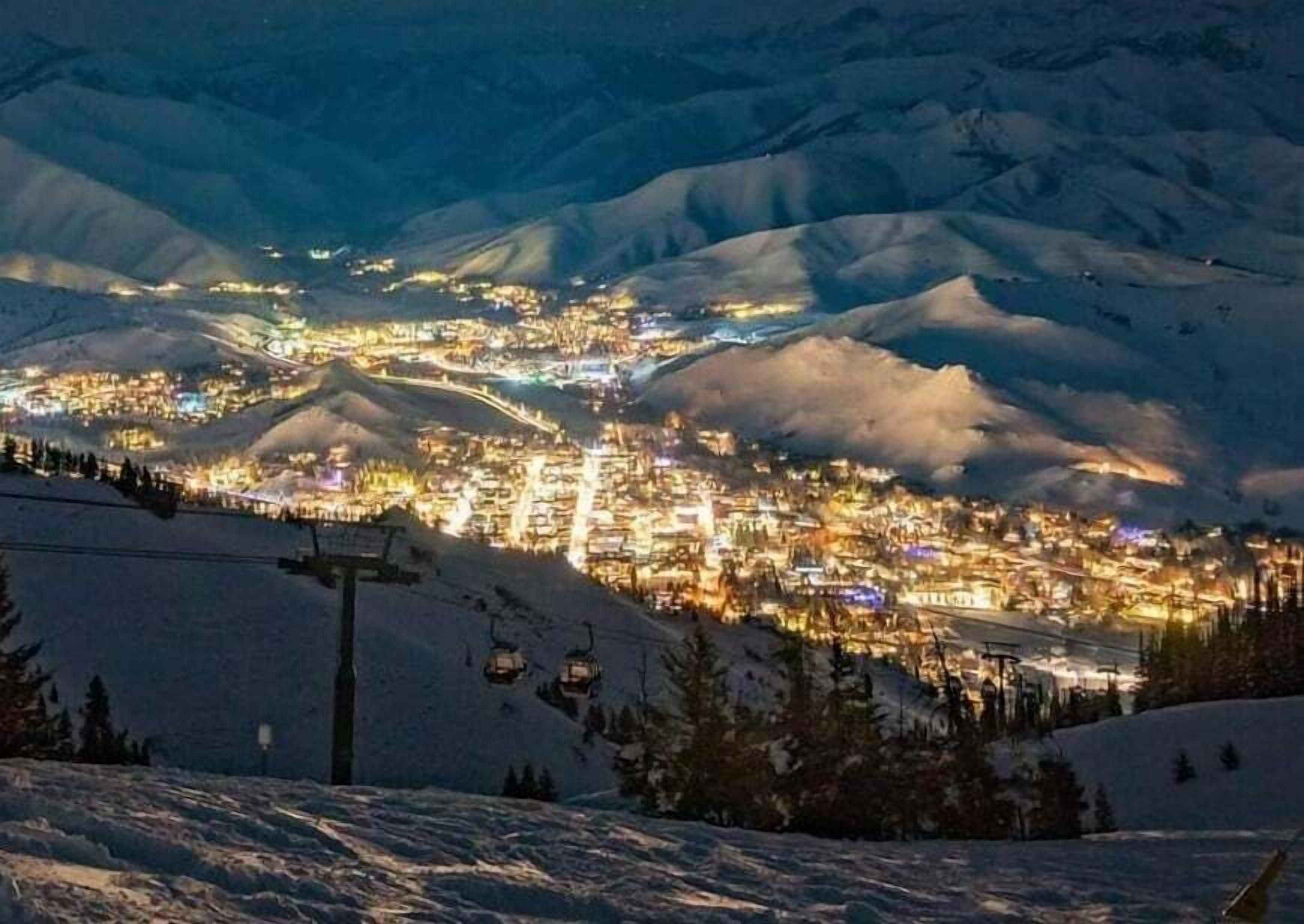 Un pueblo cubierto de nieve en la noche, con edificios iluminados y un telesilla al frente.